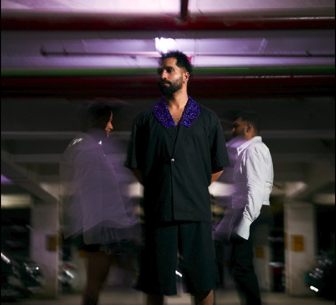 Man in a black outfit with a purple collar standing in a parking garage.
